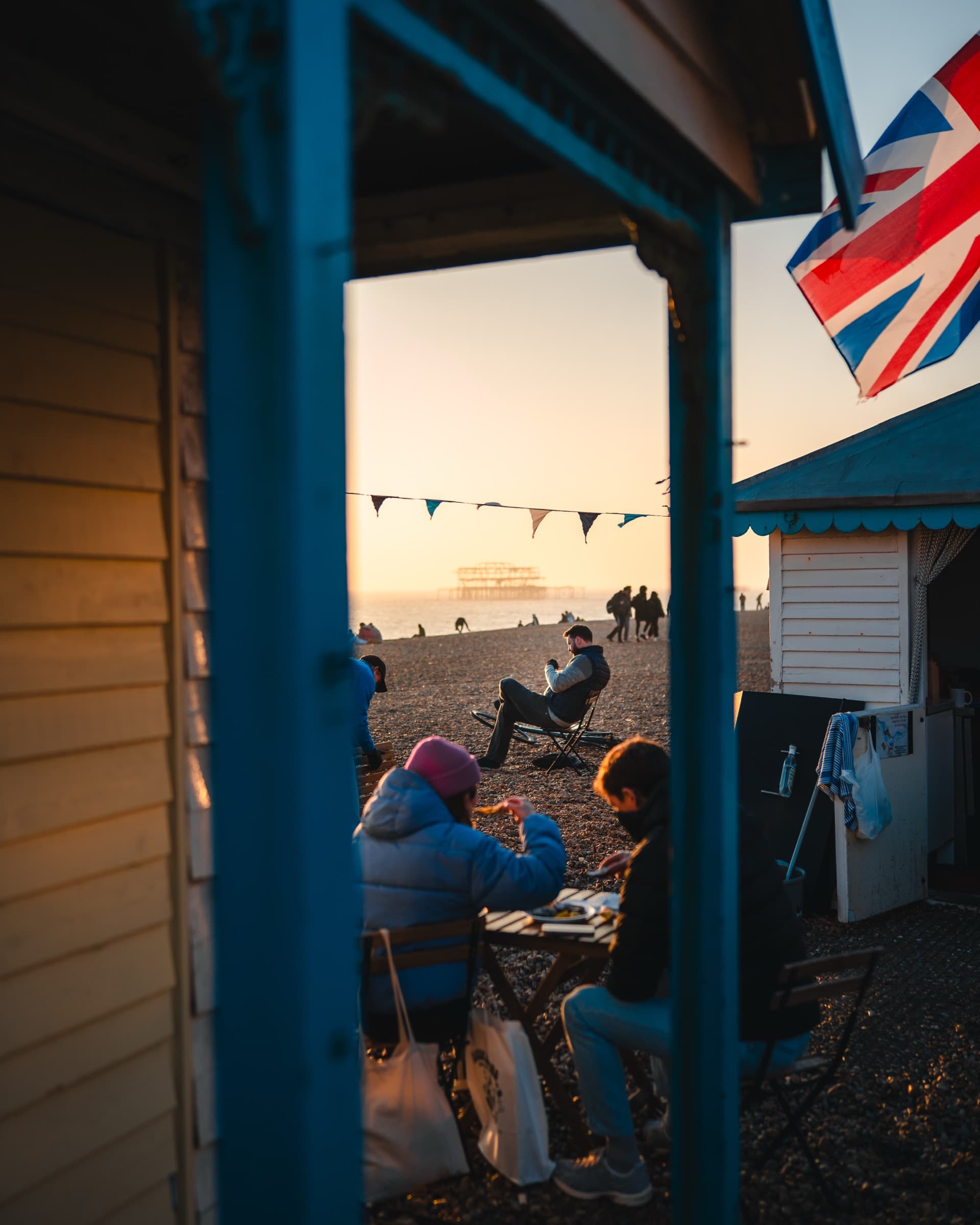 People on the beach seen between two beach huts, edited with the Made in Brighton pack