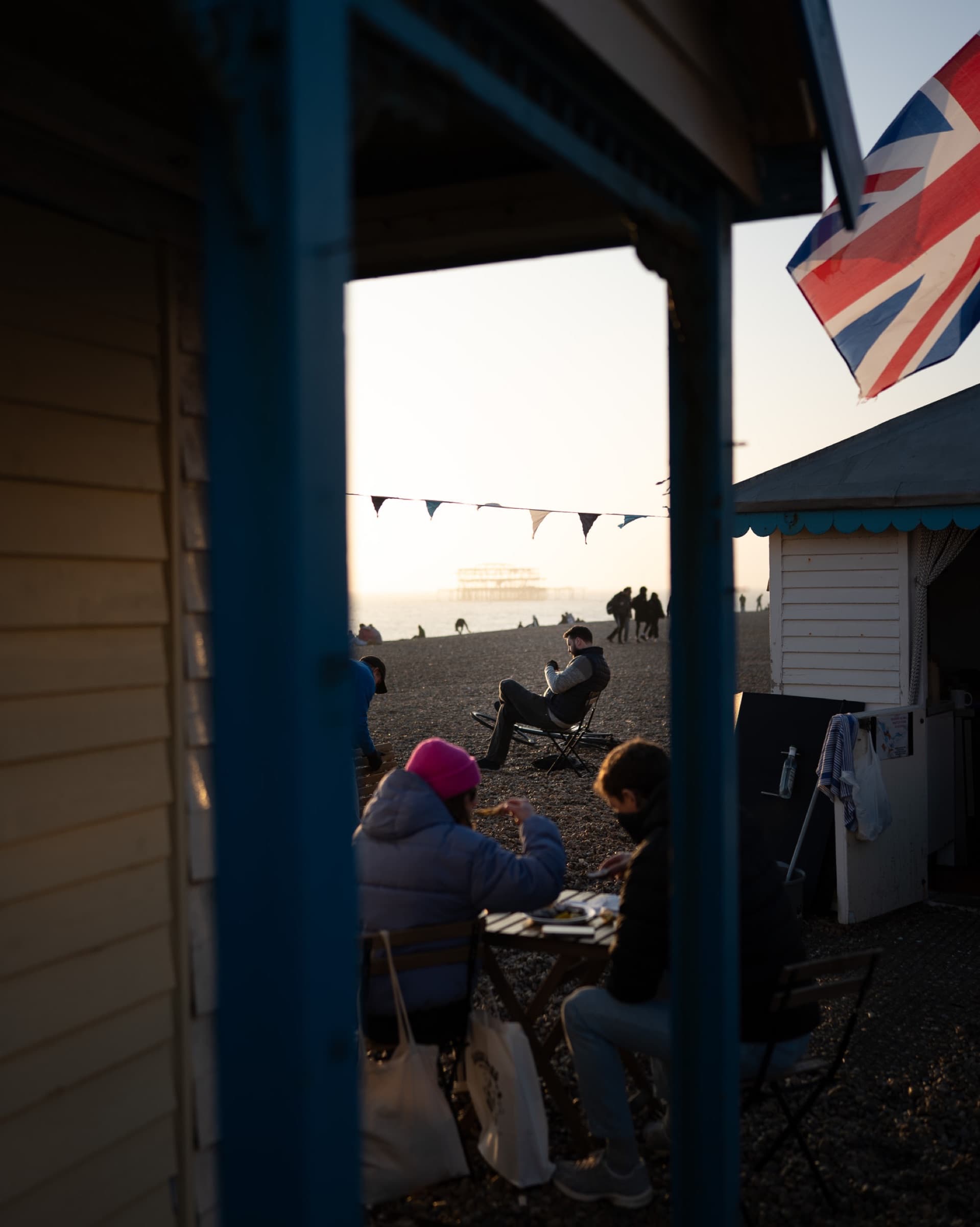 People on the beach seen between two beach huts, before editing