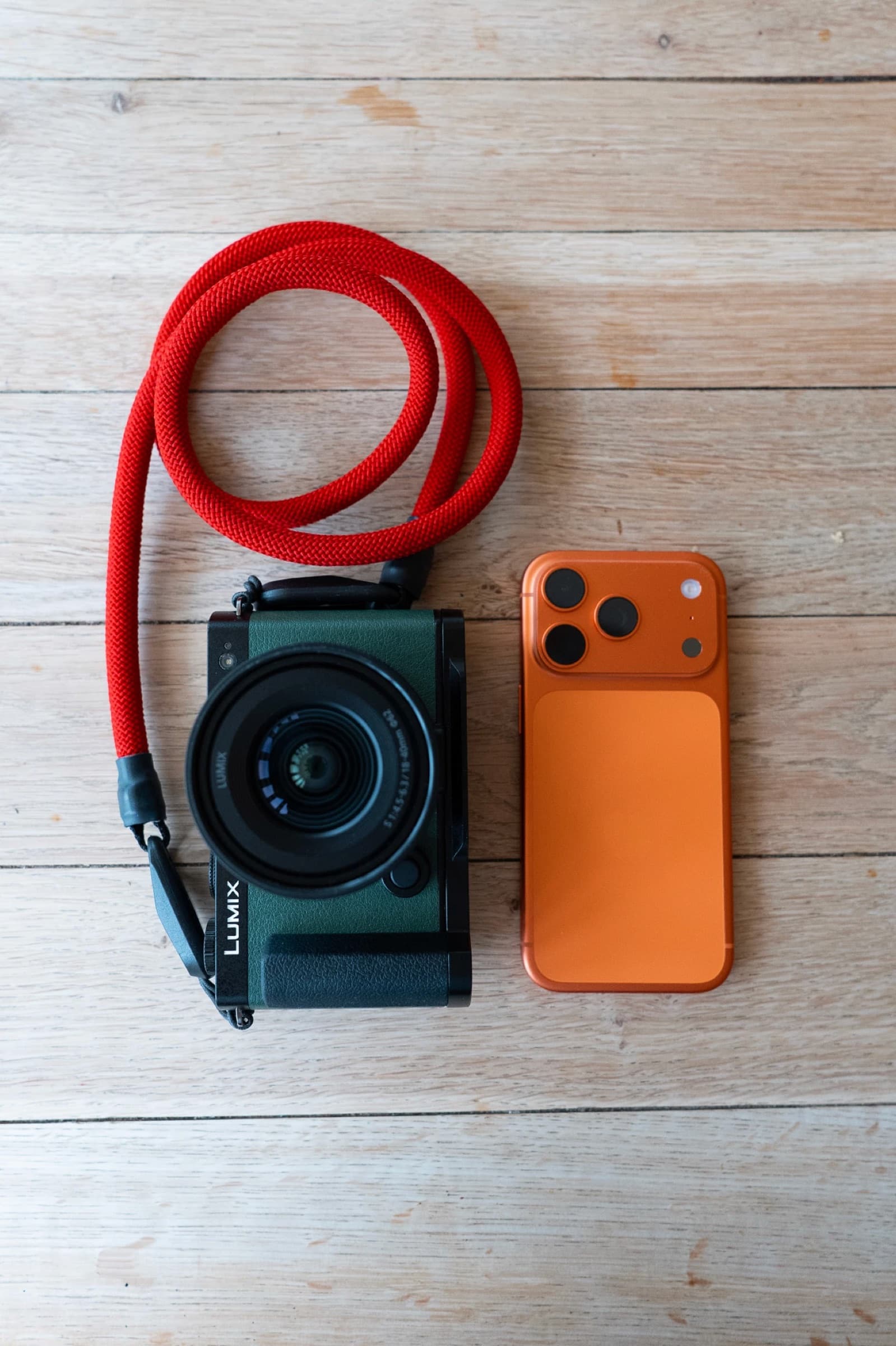 A Lumix camera and an orange iPhone on a wooden table, before editing